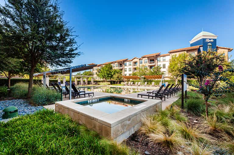 Resort pool deck with fire pit, pergola, lounge chairs, and villa buildings in background