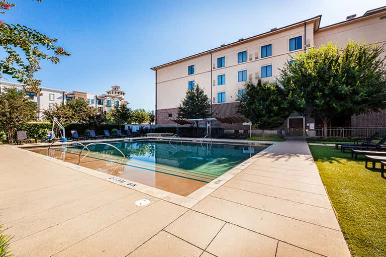 Resort pool with blue loungers, hotel building, and landscaped grounds on sunny day