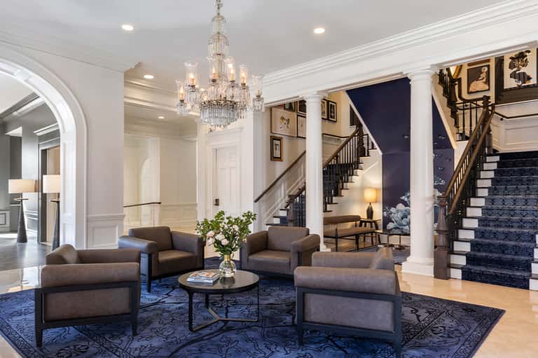 Elegant hotel lobby with crystal chandelier, neutral furniture, columns, and grand staircase