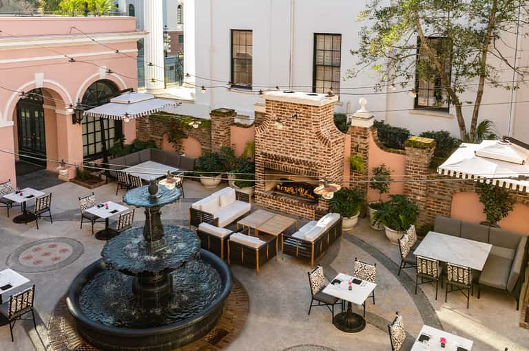 Courtyard seating area with fountain, brick walls, white umbrellas, and lounge furniture