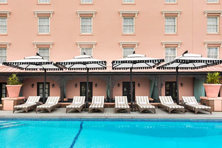 Classic hotel pool with striped umbrellas, pink building facade, and multiple lounge chairs