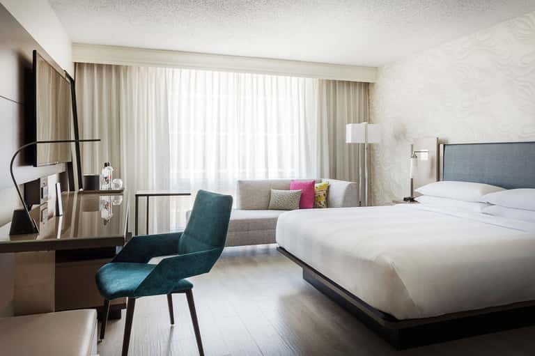 Contemporary hotel bedroom with king bed, teal accent chair, desk, flat-screen TV, and ocean view