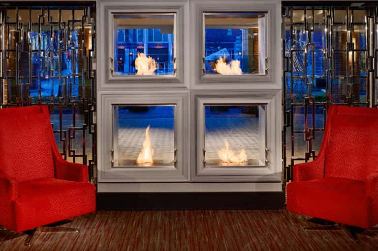 Modern fireplace with glass doors framed by red accent chairs and ocean views at dusk