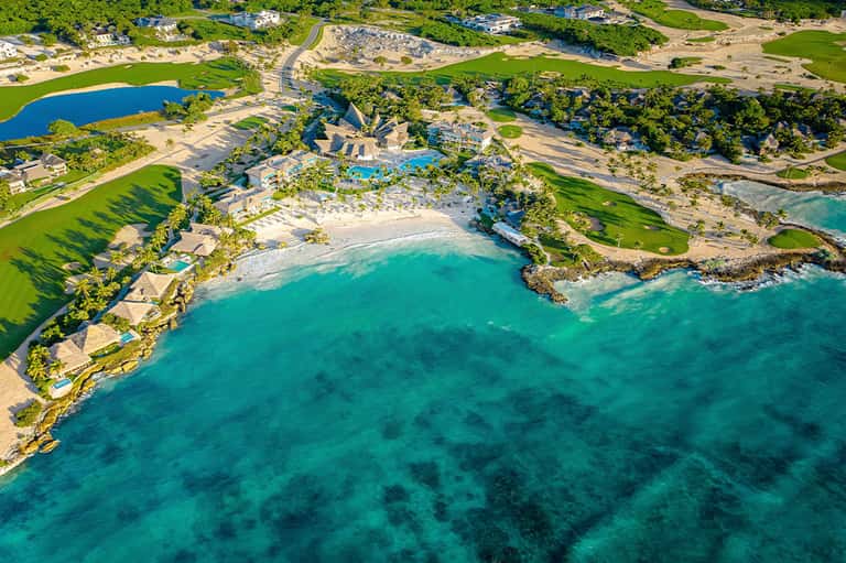 Aerial view of luxury beachfront resort with turquoise water, white sand beach, and manicured green grounds