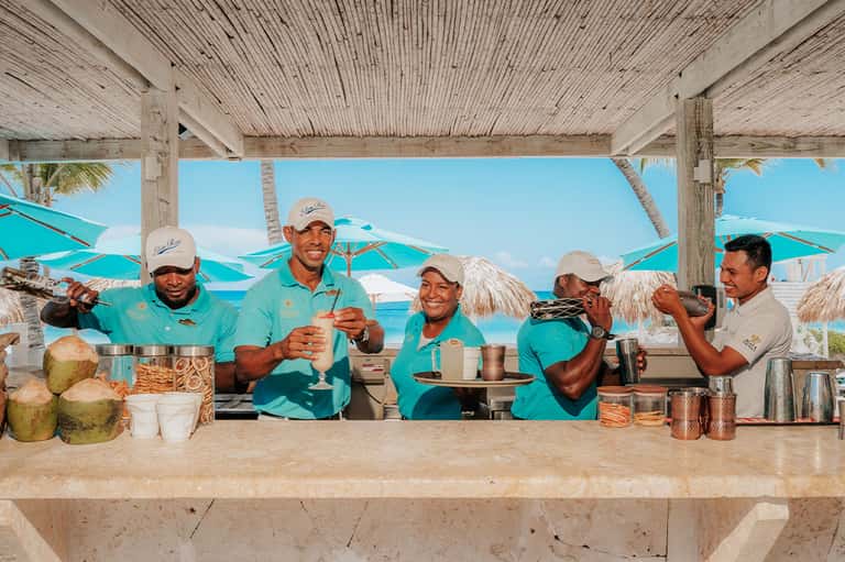 Beachside bar with staff in turquoise uniforms serving tropical drinks under thatched roof