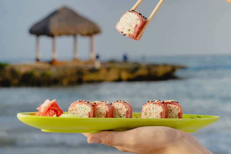 Sushi rolls on lime plate with beach gazebo and ocean in background