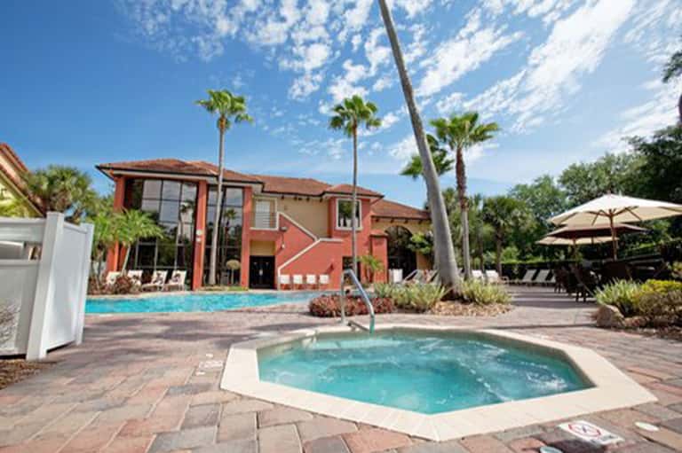 Resort main building with red exterior, pool, spa tub, and palm tree landscaping