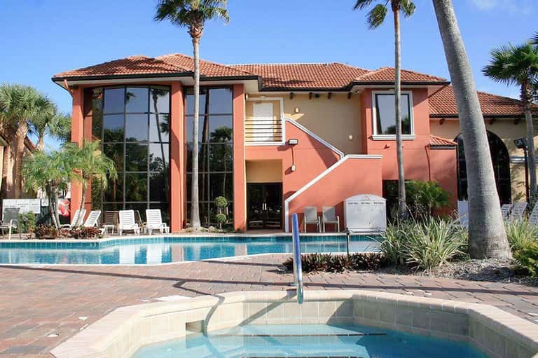 Residential pool with spa surrounded by coral-colored house and palm trees
