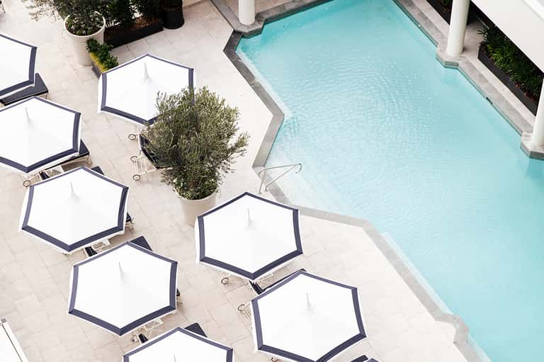Luxury hotel pool deck with hexagonal white umbrellas and crystal-blue water