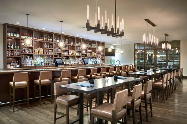 Upscale bar and lounge with dark wood shelving, elegant pendant lighting, and dining tables