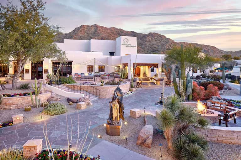 Contemporary white resort building at dusk with desert mountain backdrop and courtyard fire pit