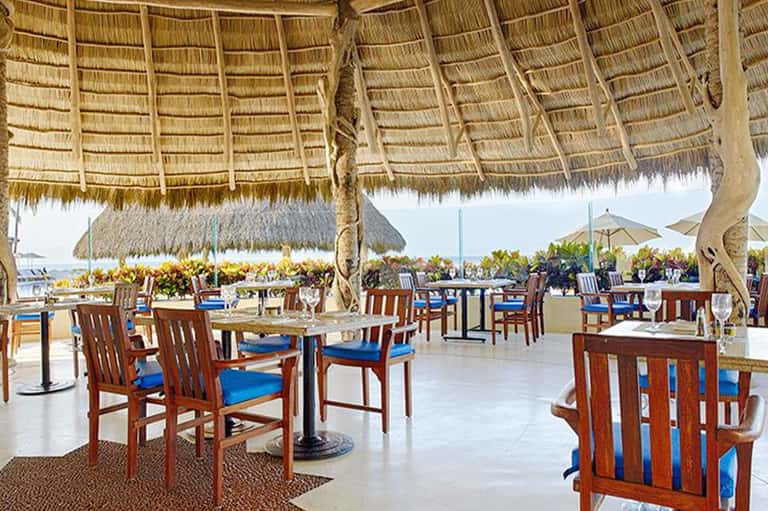 Thatched-roof beachfront restaurant with wooden chairs and ocean view