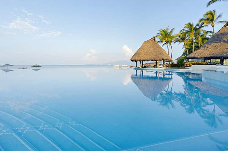 Infinity pool reflecting sky with thatched cabana and calm ocean view