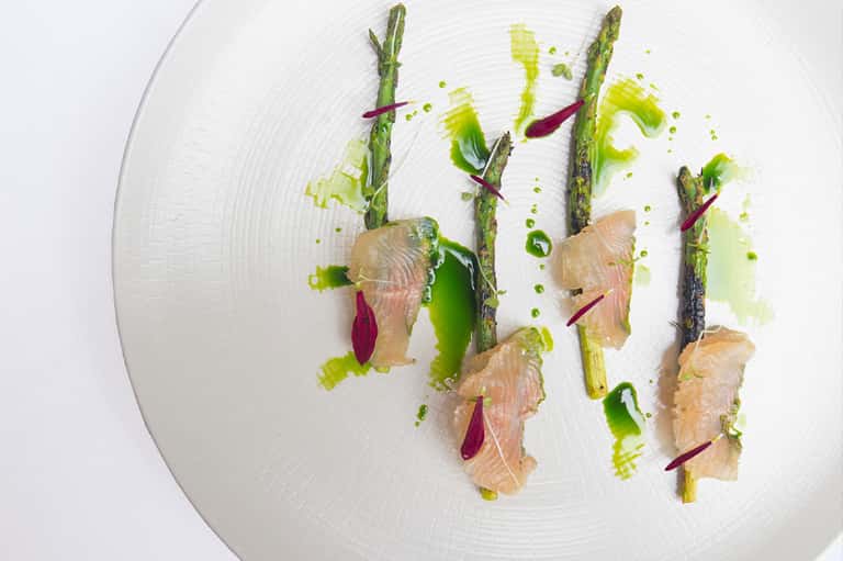 Gourmet plated dish with asparagus, smoked salmon, and green sauce on white plate