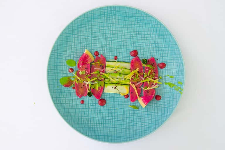 Plated dish with dragon fruit, green vegetable, and red berries on turquoise textured plate