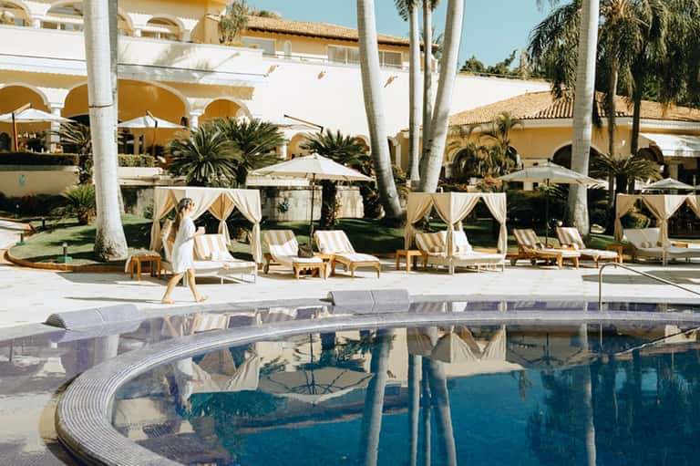 Resort pool with curved edge, striped loungers, palm trees, and yellow umbrellas