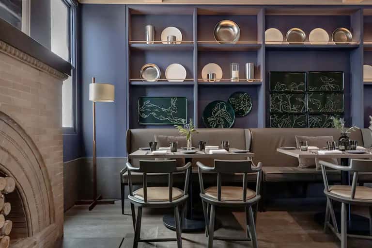 Contemporary restaurant dining area with blue-gray walls, booth seating, and decorative shelving