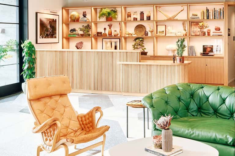 Luxury lounge with green leather sofa, tan leather chair, wooden shelving, and warm ambient lighting