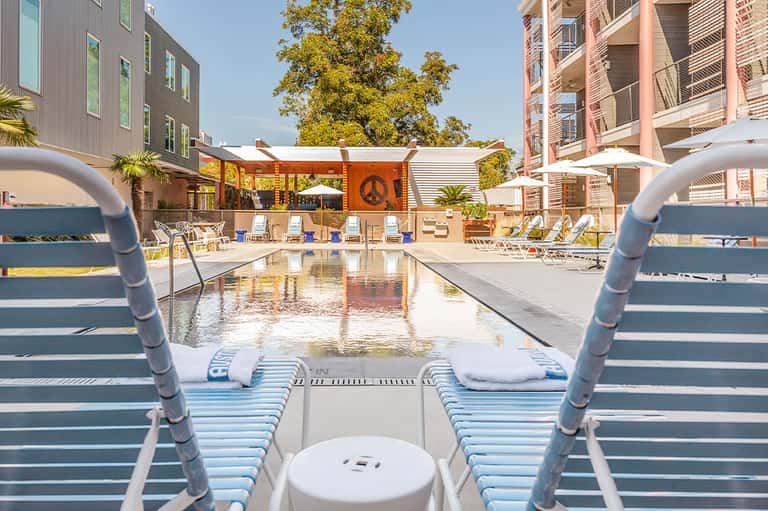 Modern resort pool with lounge chairs, peace sign wall decoration, and contemporary apartment buildings