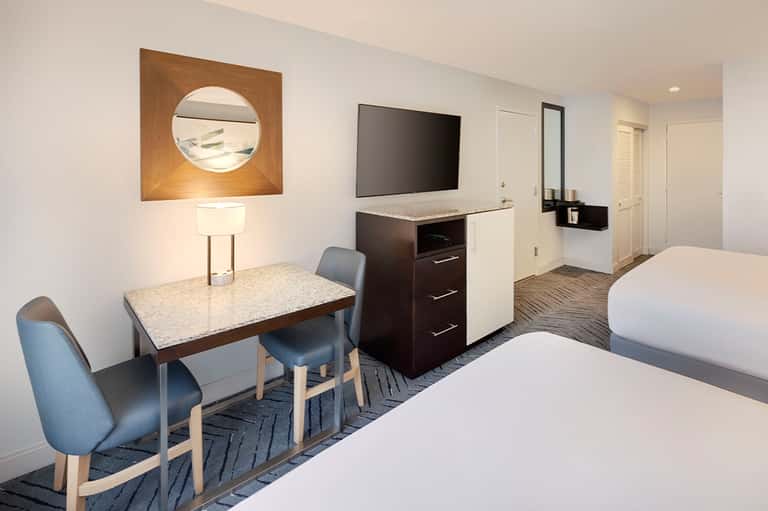 Modern hotel room with two queen beds, work desk, flat-screen TV, and contemporary furnishings