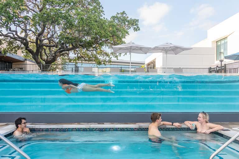 Swimmer doing freestyle strokes in lap pool with hot tub and umbrellas nearby