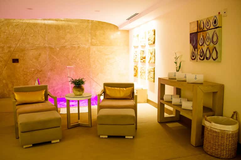 Spa relaxation room with warm golden lighting, cream chairs, wood furnishings, and decorative wall art