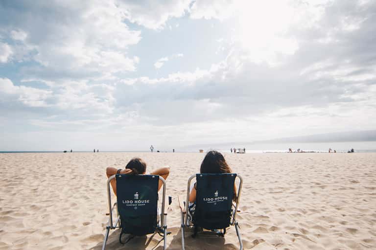 Two women relaxing in beach chairs on sandy shore facing calm ocean water