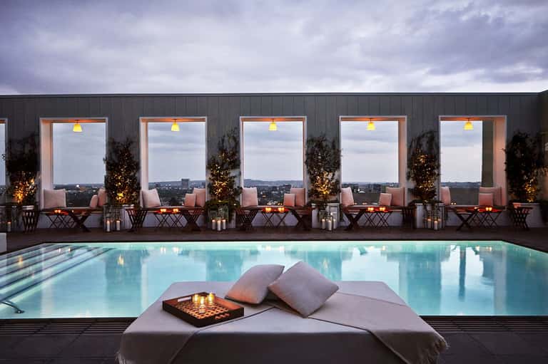 Rooftop pool at night with city skyline view, lounge seating, and ambient lighting