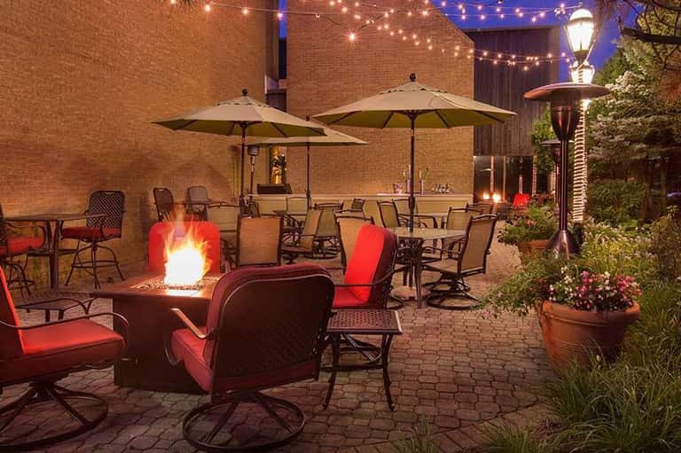 Evening courtyard patio with firepit, umbrellas, string lights, and red chairs