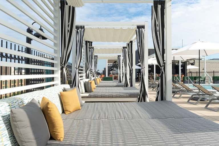 Covered cabana lounge with striped curtains, yellow and gray cushions, and rooftop pool deck with lounge chairs