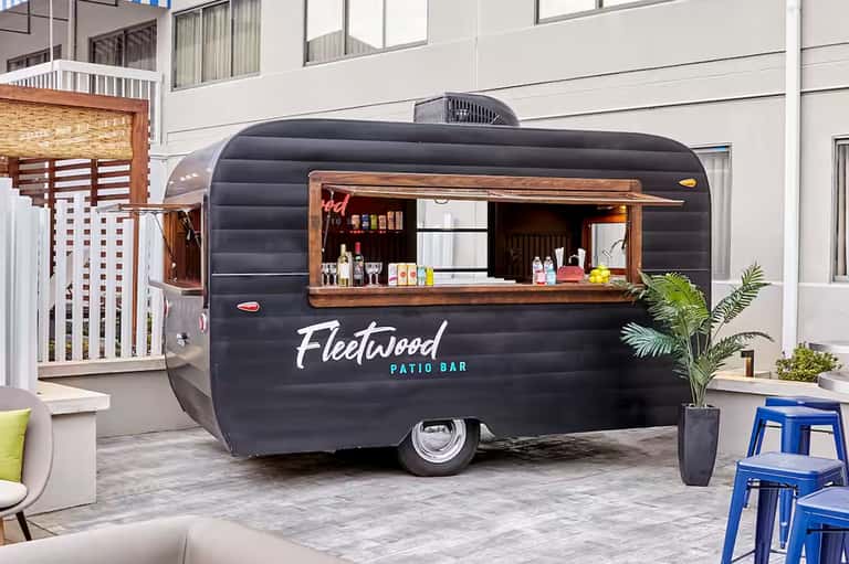Black vintage-style mobile bar trailer with wooden serving window at resort patio