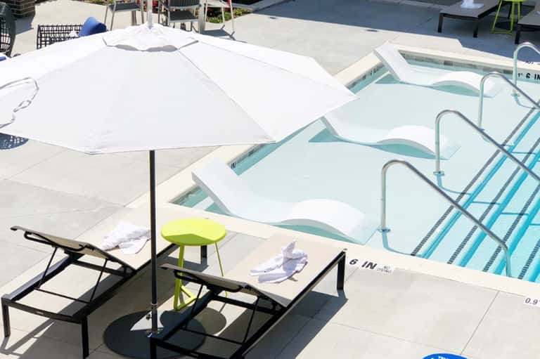 Resort pool deck with white umbrella, lounge chairs, and spa pools