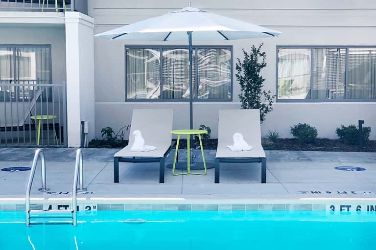 Modern poolside lounge with white loungers, umbrella, and spa building