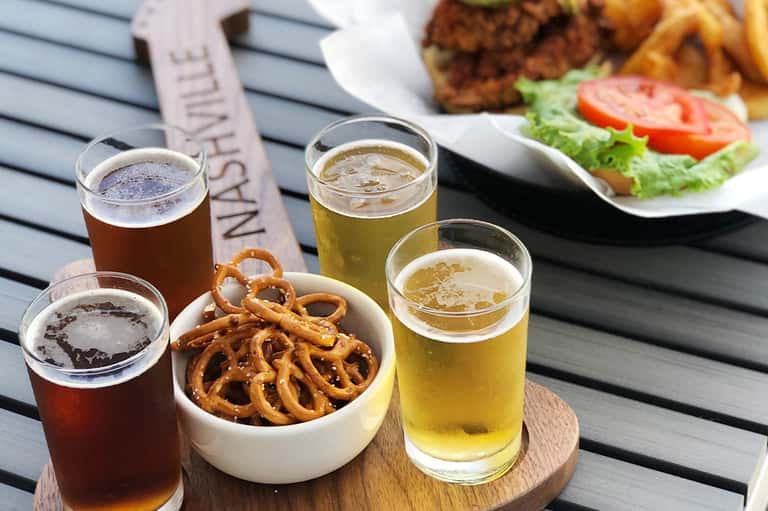 Outdoor dining with beer flights, pretzels, burger, and salad on wooden table