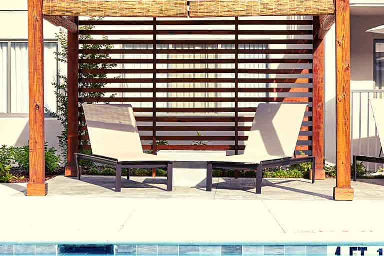 Wooden pergola with shade sails over lounge chairs beside resort pool