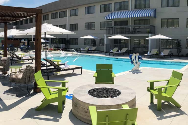 Resort pool area with blue water, white umbrellas, green lounge chairs, and fire pit seating