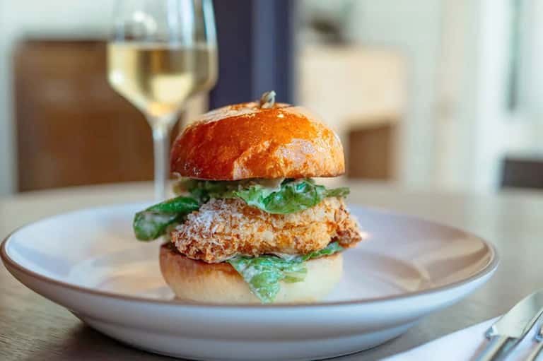Gourmet burger with greens on white plate paired with white wine