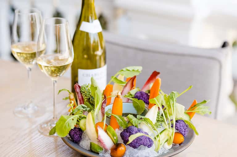 Fine dining presentation with white wine, champagne bottle, and colorful vegetable appetizer arrangement
