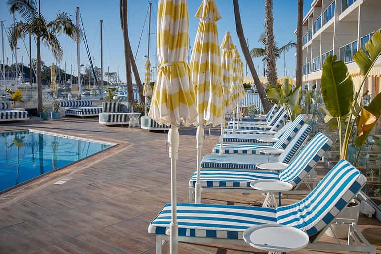 Waterfront pool with yellow and white striped umbrellas, sailboats, and marina views in background
