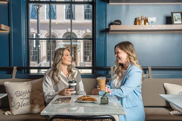 Two women chatting over coffee in a contemporary café with large windows and blue accents