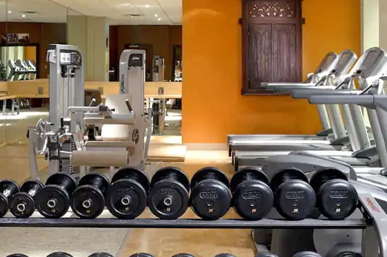 Modern hotel fitness center with dumbbells, cardio machines, and orange accent walls
