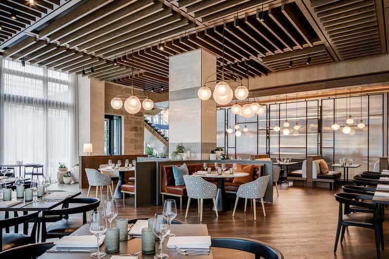 Contemporary restaurant with wooden beams, pendant lights, booth seating, and floor-to-ceiling windows