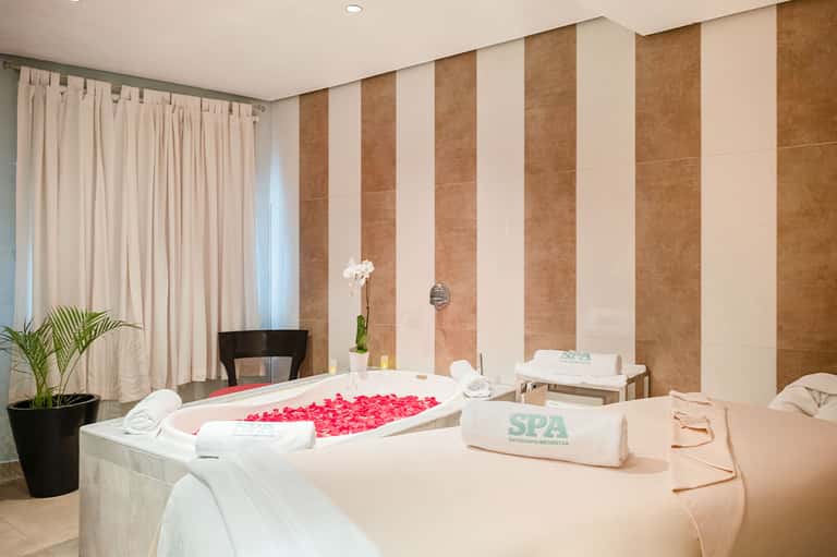 Luxurious spa bathroom with marble tub filled with red flower petals and striped tile walls