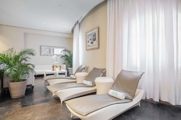 Spa relaxation room with cream-colored lounge chairs, plants, and sheer curtains