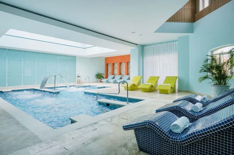 Indoor aquatic center with turquoise walls, lap pools, spa loungers, and natural skylight