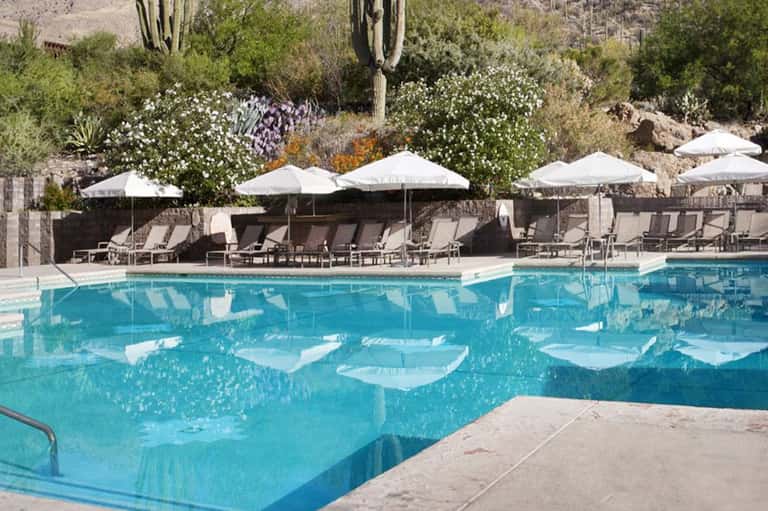Resort pool with turquoise water, white umbrellas, desert landscape with saguaro cactus backdrop