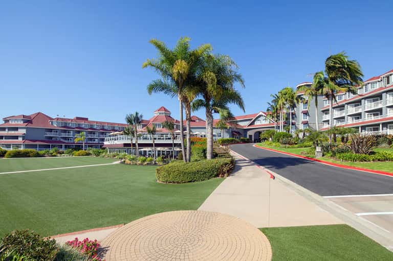 Resort entrance with golf course, palm trees, red-roofed main building, and tropical landscaping