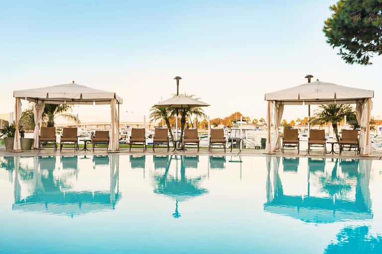 Luxurious poolside cabanas with sheer curtains and lounge chairs reflected in calm turquoise water