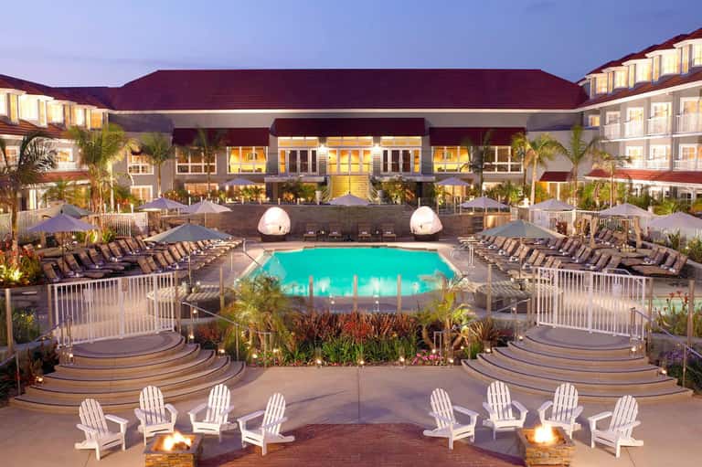 Resort pool at twilight with turquoise water, loungers, fire pits, and illuminated main building