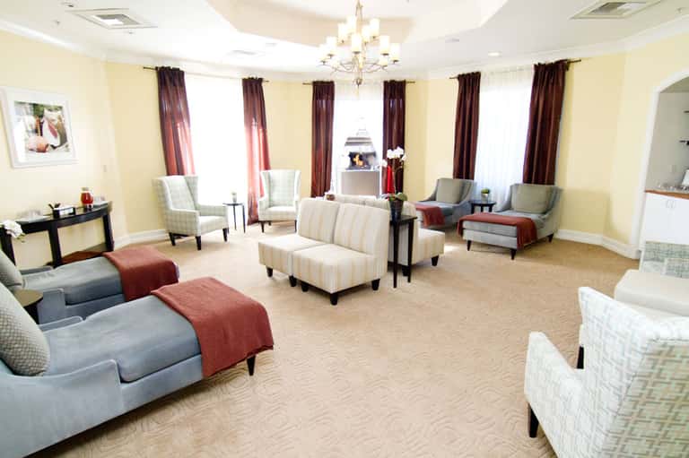 Elegant hotel lounge with cream seating, burgundy accents, chandelier, and multiple windows with drapes